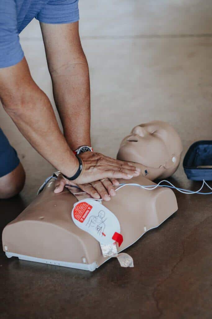 pexels-photo-11655091 Hands demonstrating CPR technique on a training mannequin with AED.